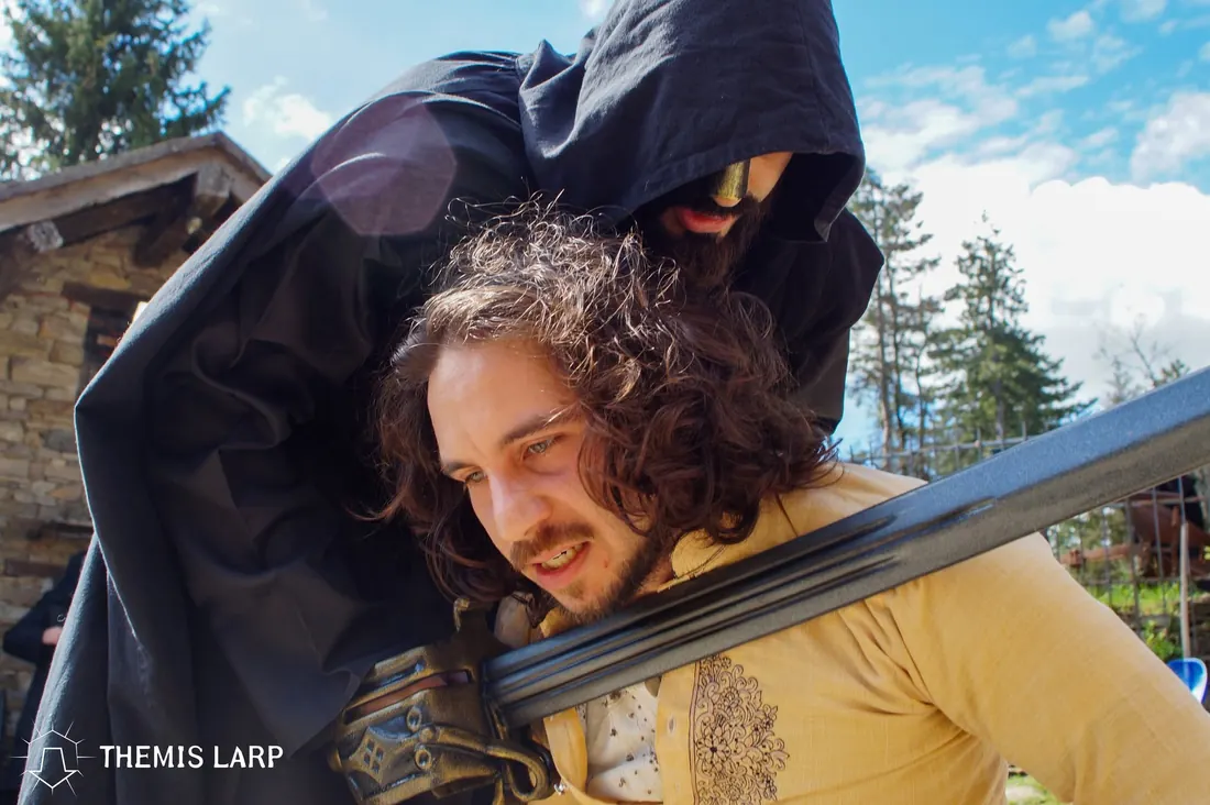 Momento di tensione narrativa durante un evento Themis, con un personaggio minacciato da una lama scenica